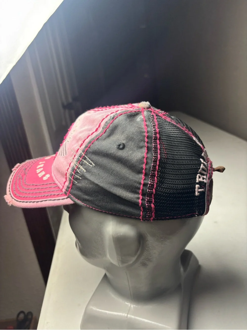 pink, distressed True Religion brand jeans cap with embroidered wings and a logo
